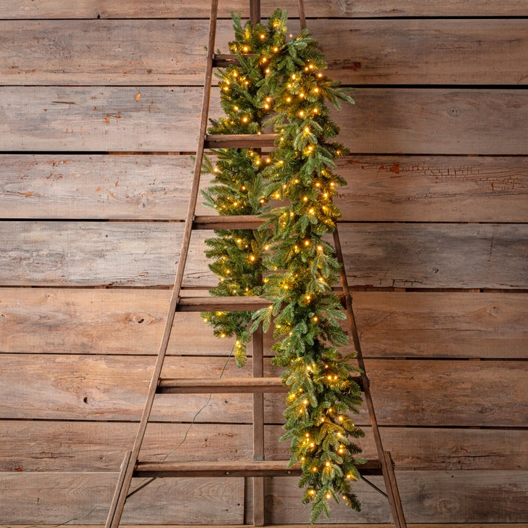 Douglas Fir 9-foot pre-lit garland with warm white lights draped over a rustic wooden ladder.