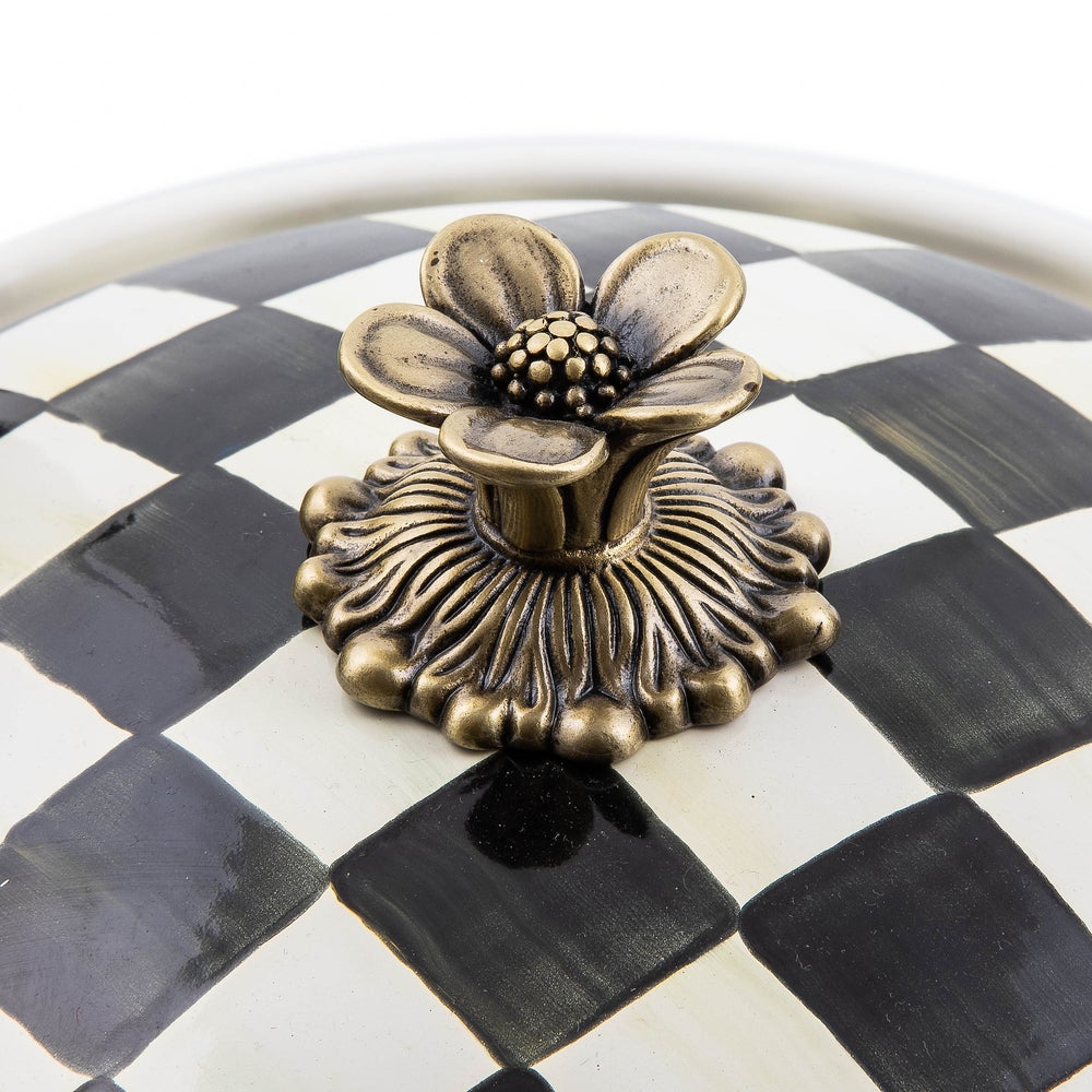 Close-up of an antiqued brass flower-shaped knob on a black and white checkered casserole lid.