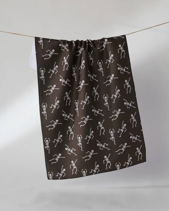 Black waffle weave tea towel with a white dancing skeleton pattern hanging on a clothesline.