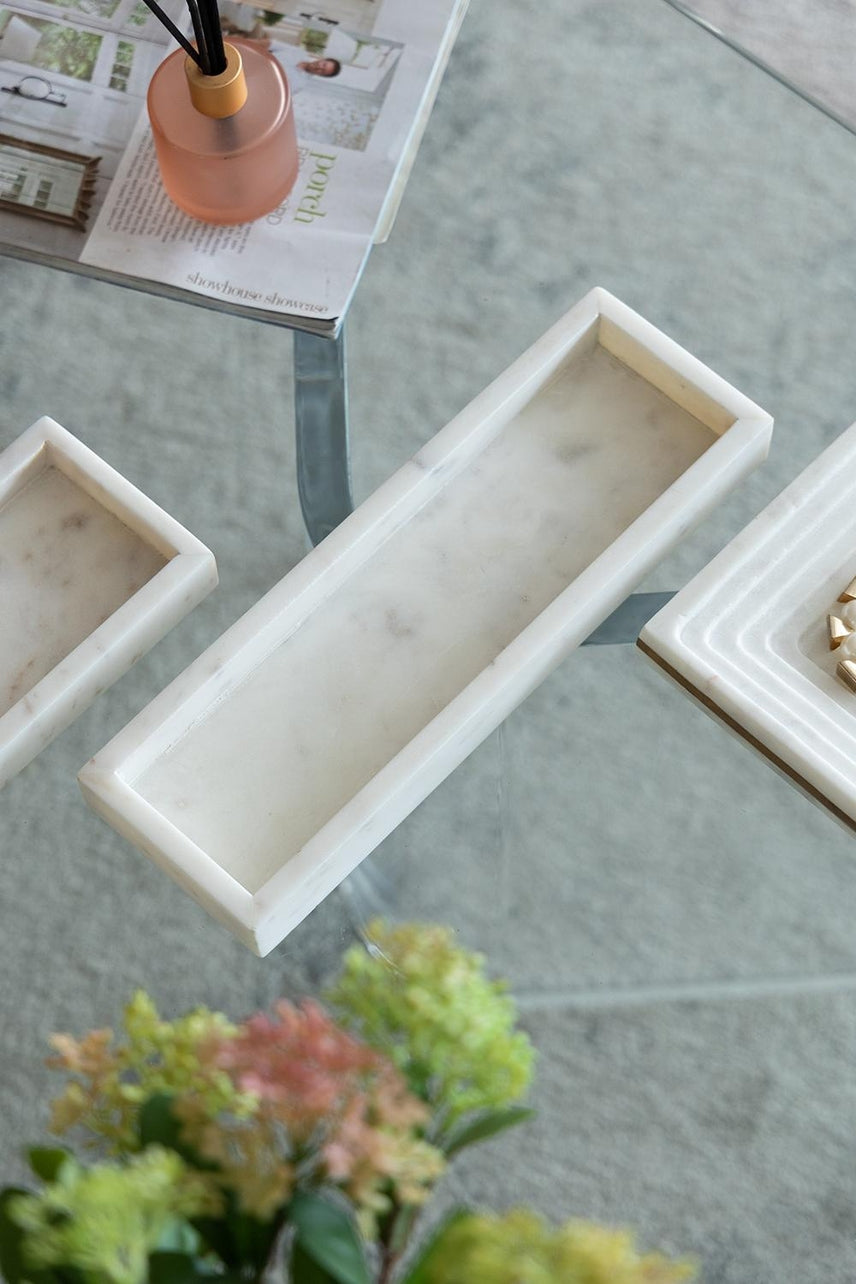 Long rectangular white marble tray with natural grey veining on a glass table.