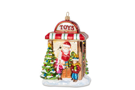 Handcrafted blown glass ornament of Santa's toy shop with children and a Christmas tree.