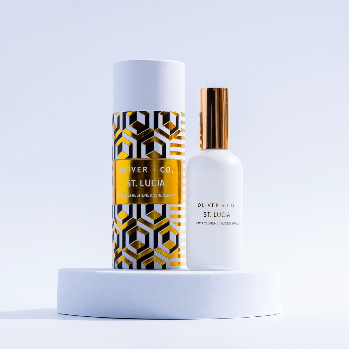 Oliver + Co. St. Lucia Room Refresher and Linen Spray bottle with gold-patterned cylinder packaging.