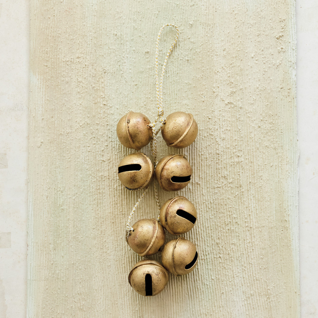 Cluster of eight gold metal jingle bells hanging from a white and gold braided cord.