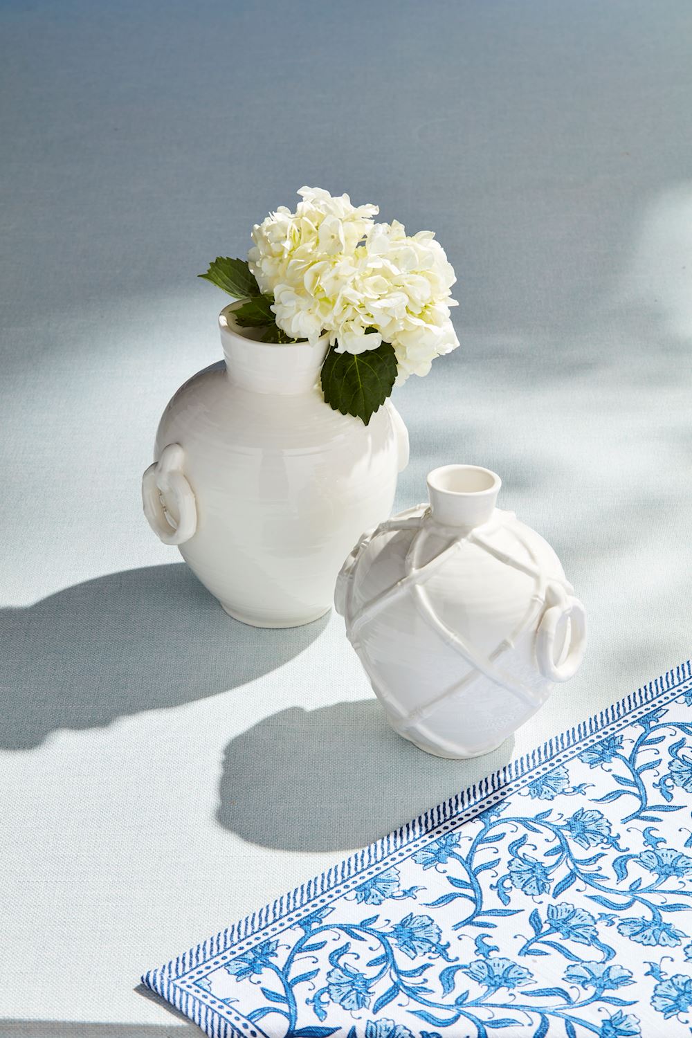 White stoneware bamboo vase with side ring handles and textural detail next to a floral vase.
