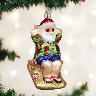 Sunning Santa glass ornament wearing a floral shirt and sunglasses, sitting on a glittery beach.
