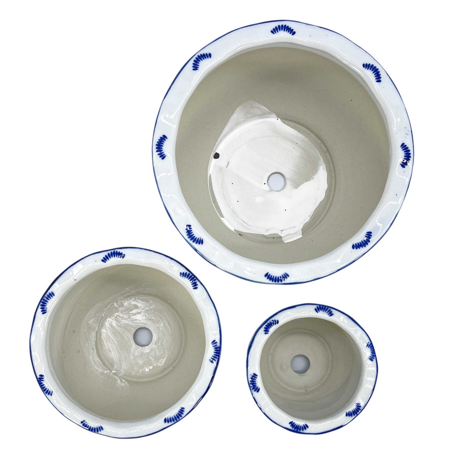 Top view of three blue and white floral ceramic pots with ruffled lips and drainage holes.