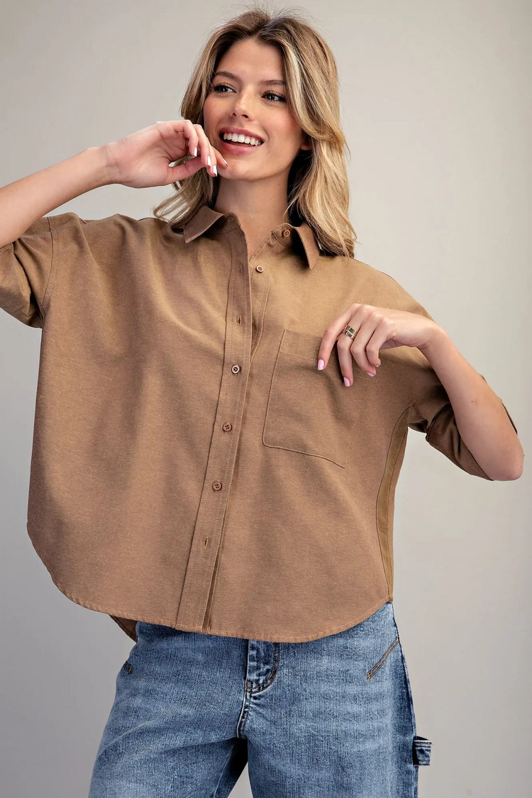 Woman wearing a brown oversized short sleeve button-down shirt with a chest pocket and blue jeans.