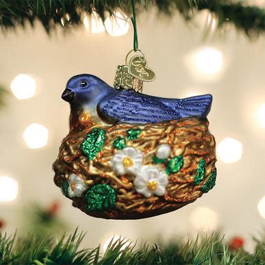 Blue bird in a golden nest glass ornament with white flowers and green glitter leaves.