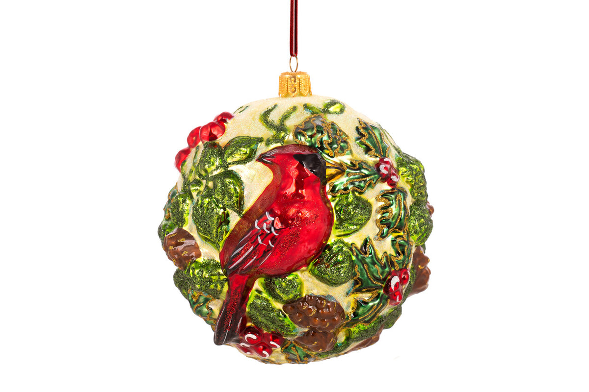 Handcrafted blown glass ball ornament featuring a red cardinal among green holly and pinecones.