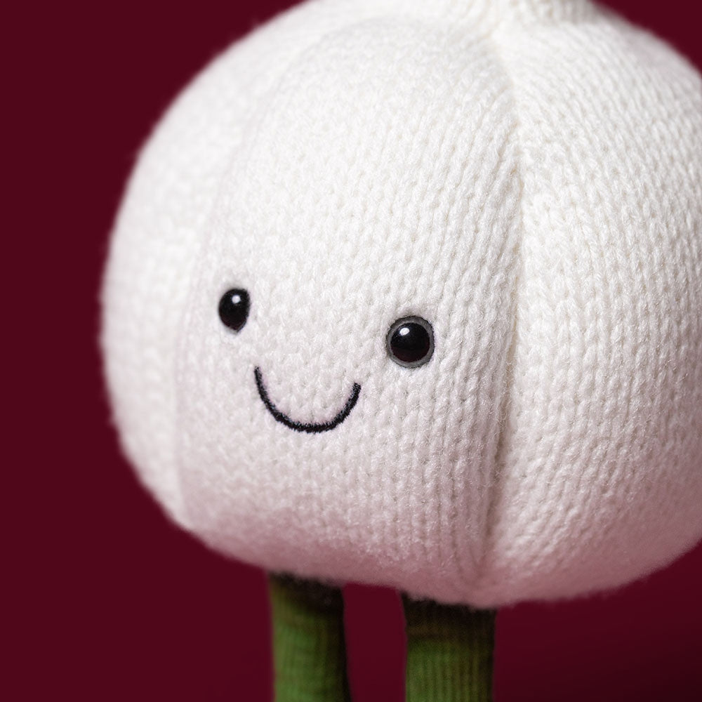 Close-up of a white knitted garlic plush toy with a smiling face and green corduroy legs.