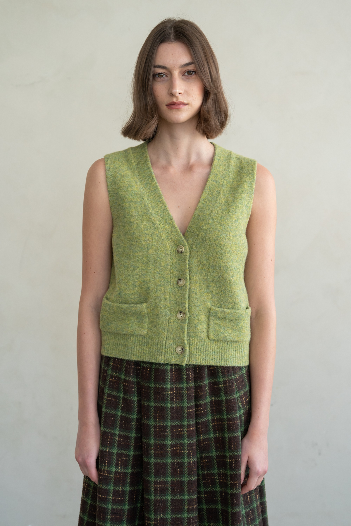 Woman wearing the Abby green knit pocket vest with a V-neckline and button-front closure.