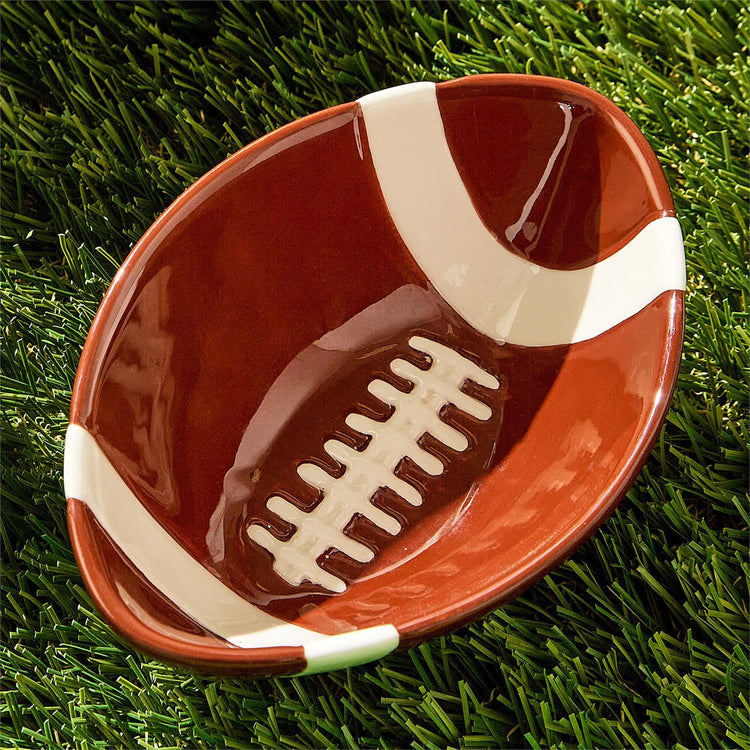 Football-shaped ceramic tidbit bowl with white laces and stripes on green artificial turf.