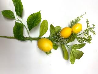 Artificial lemon pick with three yellow lemons and green leaves on a white background.