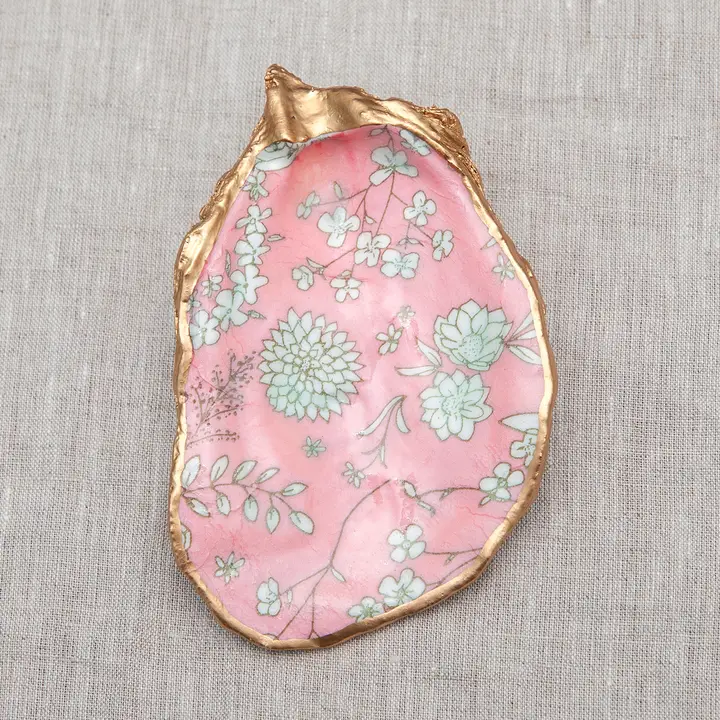 Decoupaged oyster shell with pink floral pattern and metallic gold trim on a linen background.