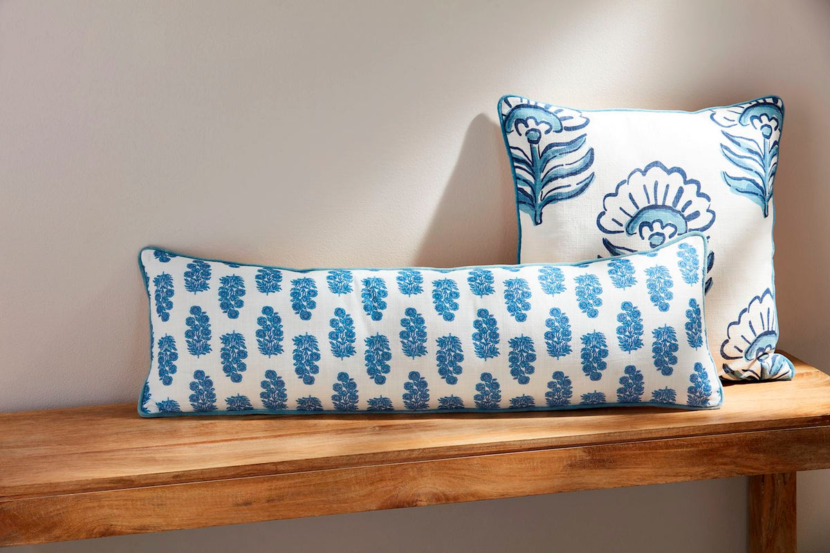 Blue block print long pillow and matching square pillow on a wooden bench against a neutral wall.
