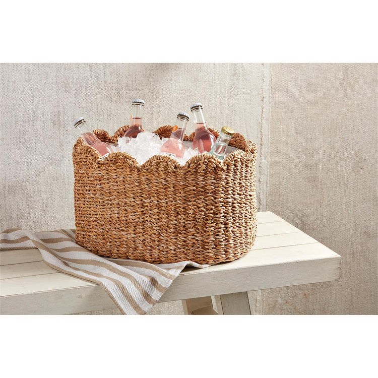 Woven seagrass party tub with a scalloped rim, filled with ice and bottled drinks on a white bench.