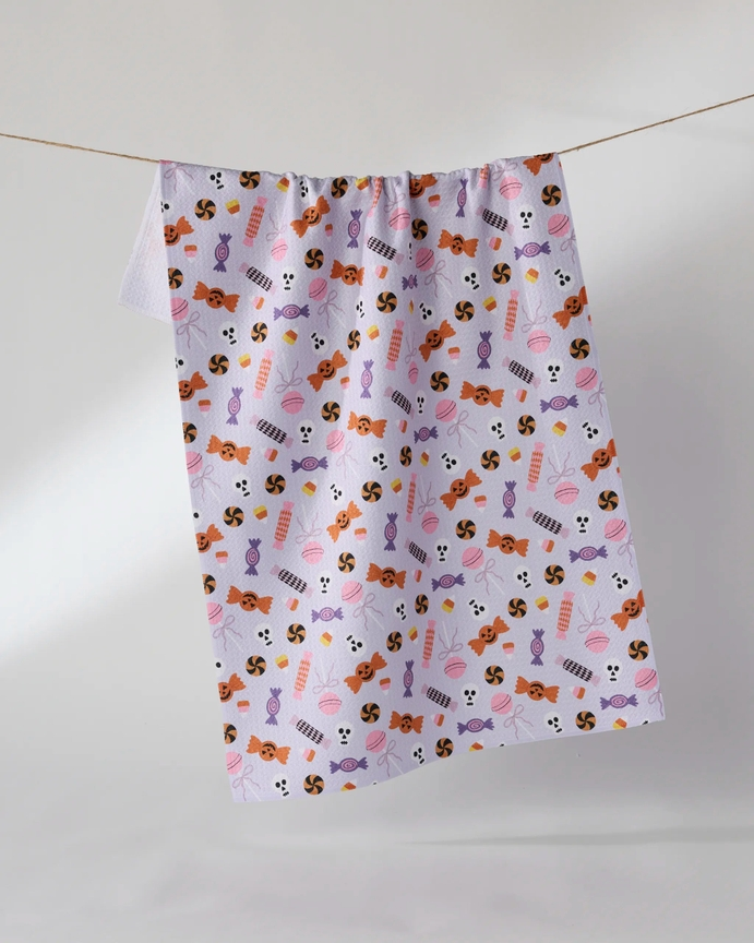 Waffle weave Halloween tea towel with a pattern of candy, skulls, and lollipops on light purple.