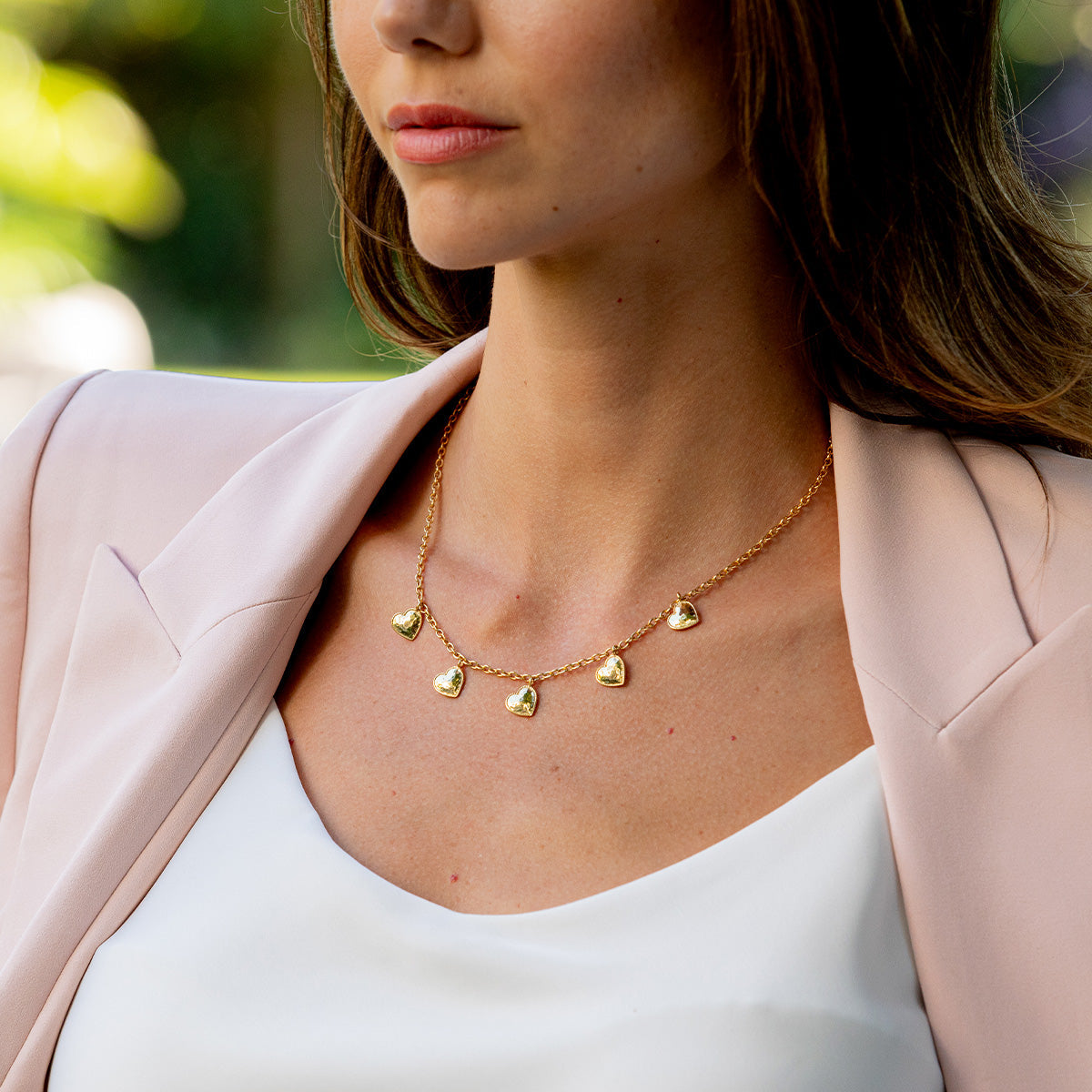 Woman wearing a gold multi-station necklace with five hammered heart charms on a delicate chain.