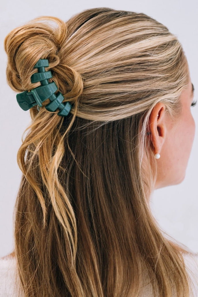 Small dark green classic hair clip holding a blonde woman's hair in a half-up hairstyle.