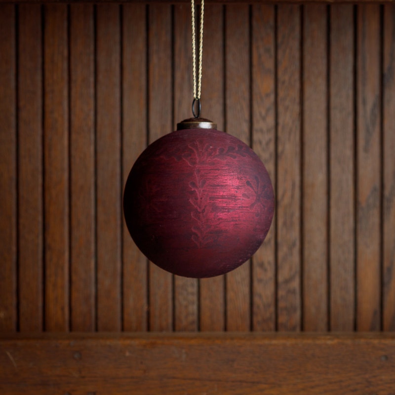 5-inch frosted cranberry glass ball ornament with etched floral patterns hanging by a gold string.