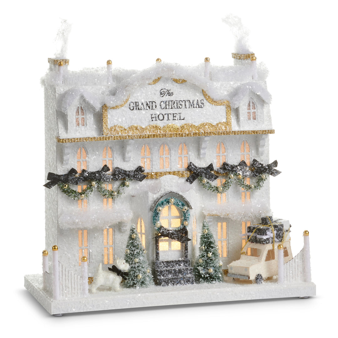 14.5 inch lighted paper Grand Christmas Hotel with snow, trees, a dog, and a car with gifts.