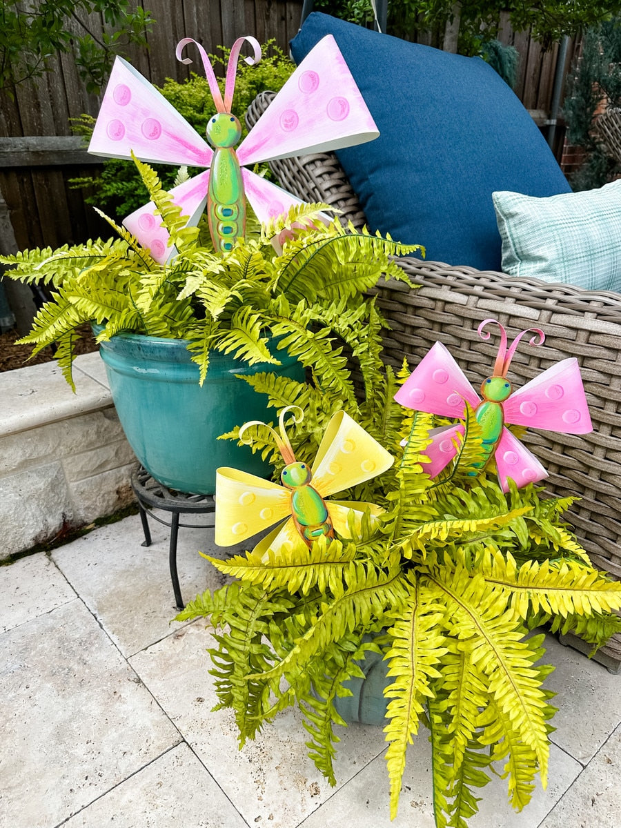 Large pink and yellow metal butterfly garden stake with polka dots, nestled in ferns.