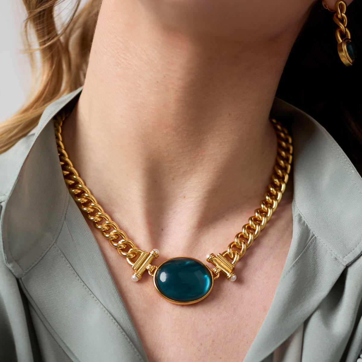 Woman wearing a Dolce Statement Necklace with 24K gold chain and a large oval teal glass pendant.