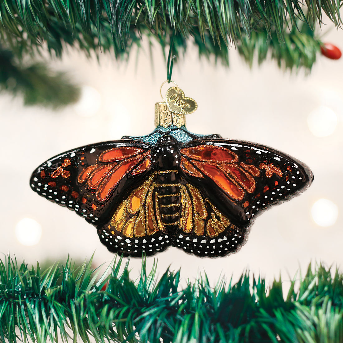 Glass monarch butterfly ornament with orange and yellow wings hanging on a green Christmas tree.