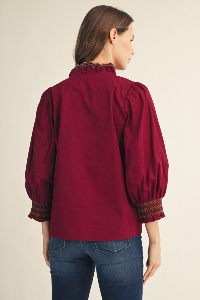 Back view of a woman wearing a burgundy top with puff sleeves and embroidered smocking cuffs.