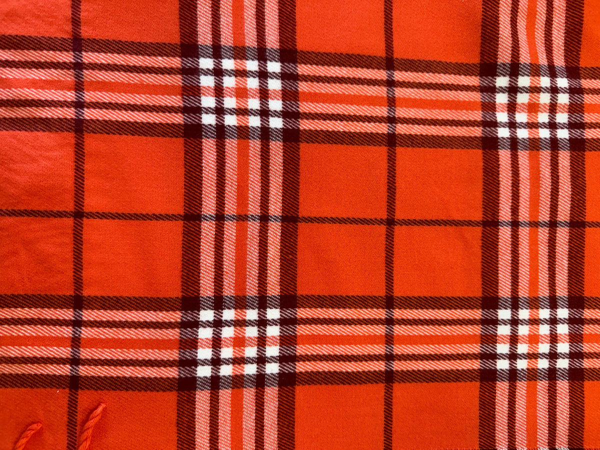 Close-up of a Scottish plaid cashmere scarf in bright orange with white and dark brown stripes.