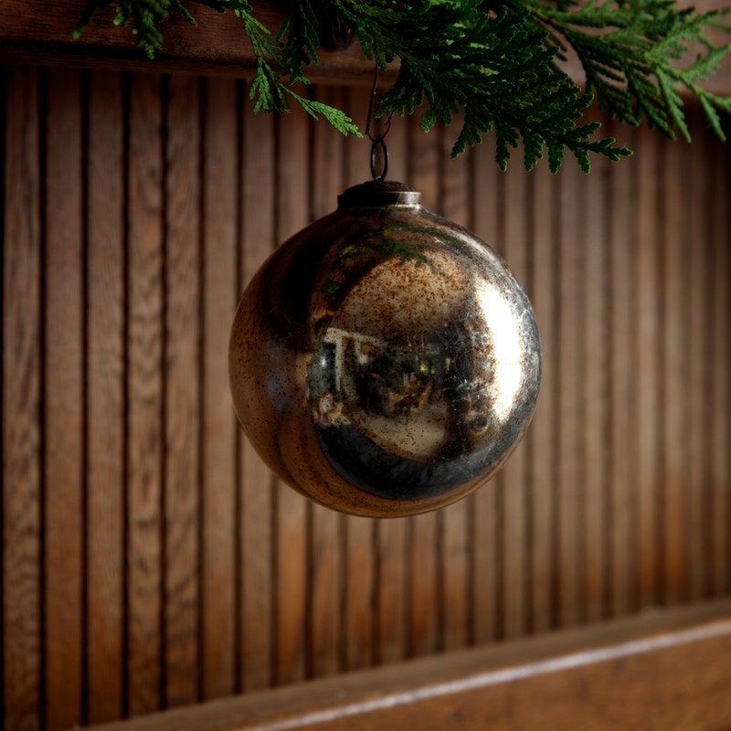 5-inch vintage gold glass ball ornament hanging from a green pine branch against a wood background.