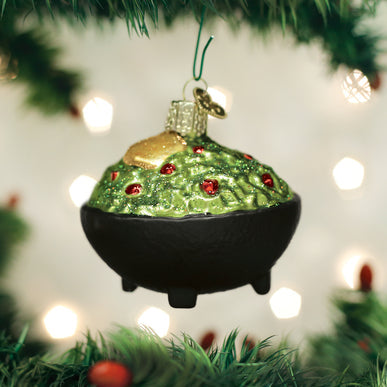 Glass guacamole ornament in a black molcajete bowl hanging on a Christmas tree.