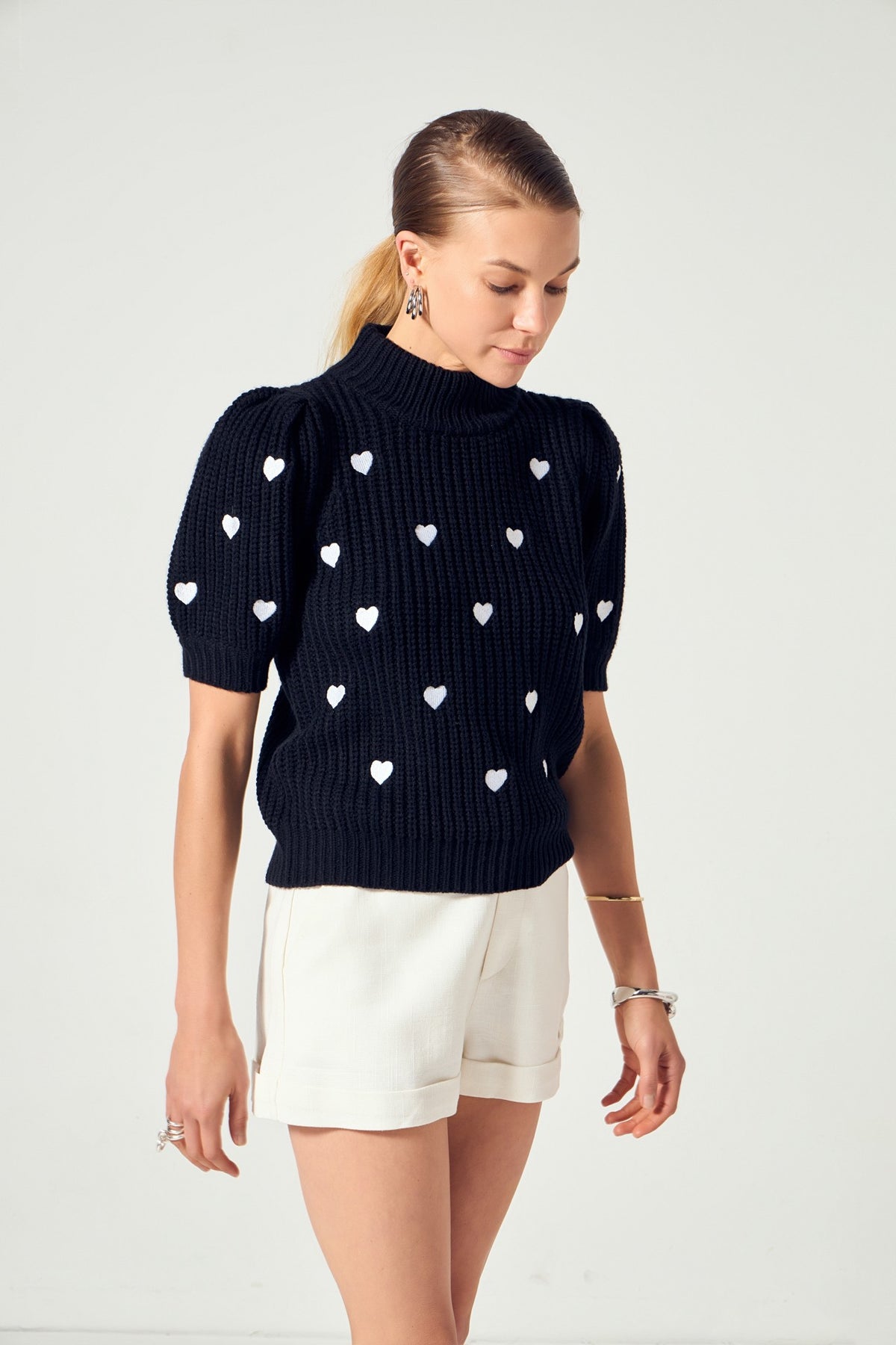 Woman wearing the Sierra black mock neck sweater with white heart embroidery and puffy sleeves.