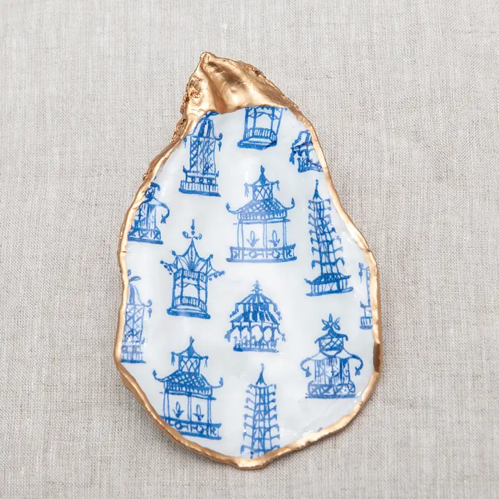 Decoupaged oyster shell with blue pagoda pattern and metallic gold trim on a neutral fabric.