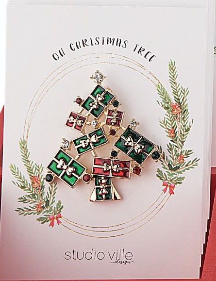 Metal Christmas tree pin with green foliage and red ornaments on a silver background.