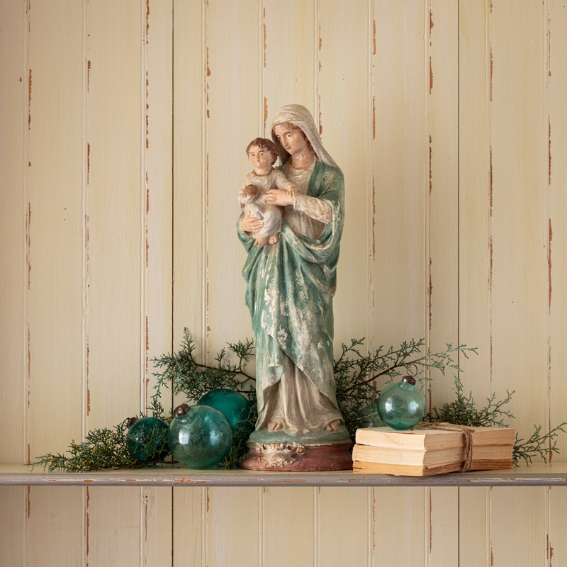 A 22-inch resin Madonna and Child statue with an aged finish on a shelf with Christmas decor.
