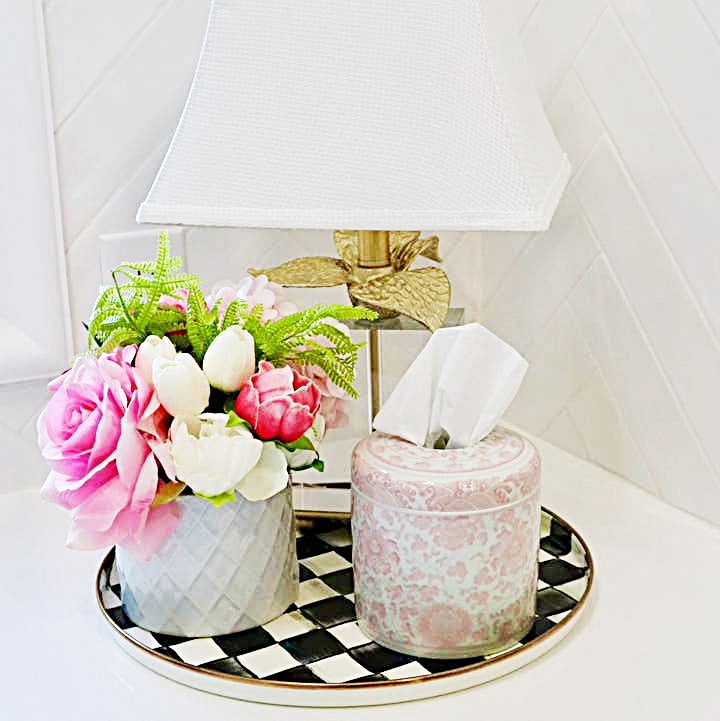 Pink and white patterned ceramic tissue vessel on a checkered tray next to a floral arrangement.