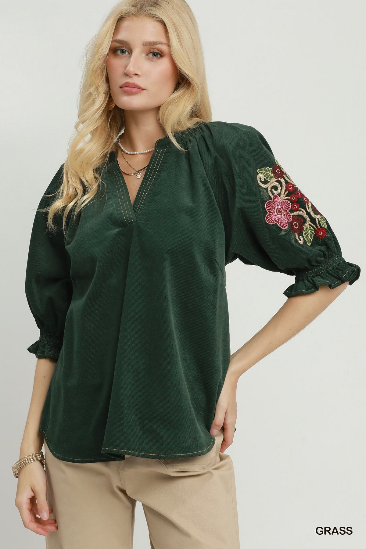 Woman wearing a dark green Eliana corduroy blouse with floral embroidery on the puff sleeves.