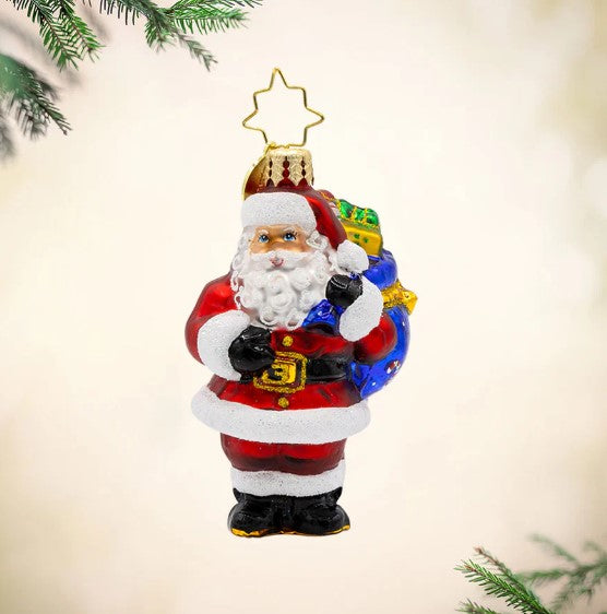 Glass Santa Claus Christmas ornament holding a blue sack of gifts with a gold star hanger.