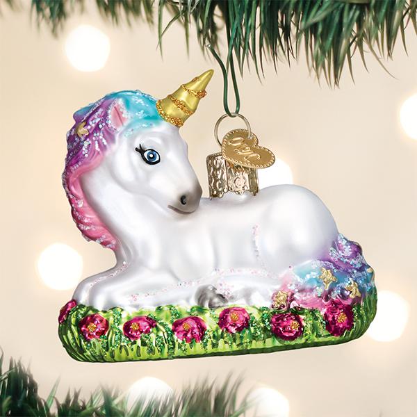 Baby unicorn glass ornament with a gold horn and colorful mane resting on a bed of pink flowers.