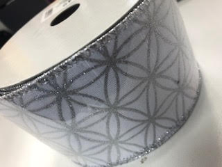 A spool of white ribbon featuring a silver metallic geometric flower pattern and glittery edges.