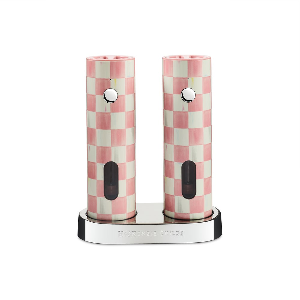 Two pink and white checkered electric salt and pepper grinders on a silver charging base.