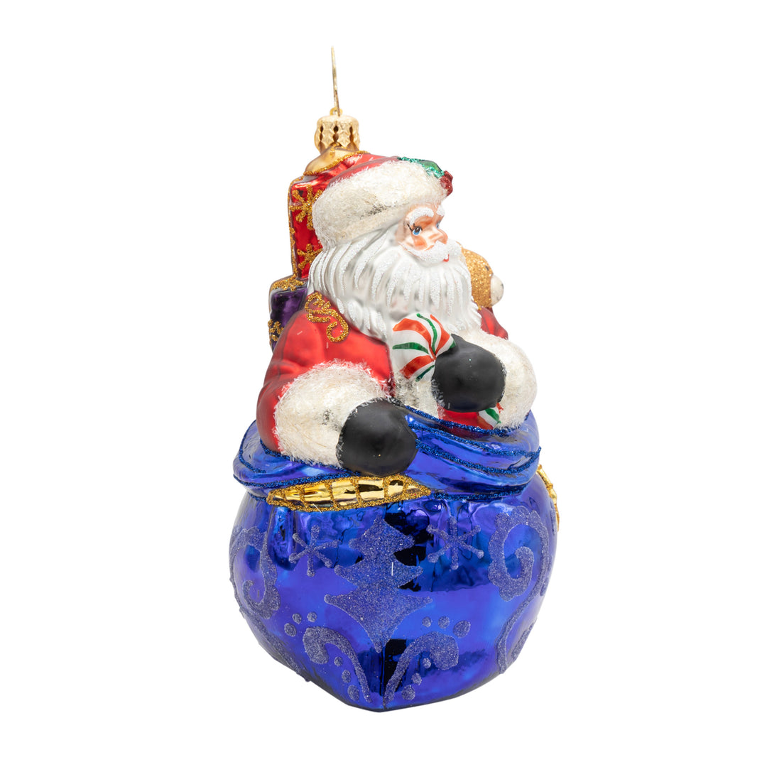 Kris Kringle glass ornament featuring Santa in a blue sack with a candy cane and gifts.
