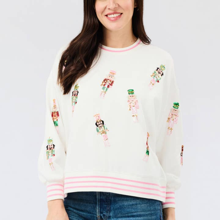 Woman wearing the Millie white sweatshirt with pink stripes and sequined nutcracker embroidery.
