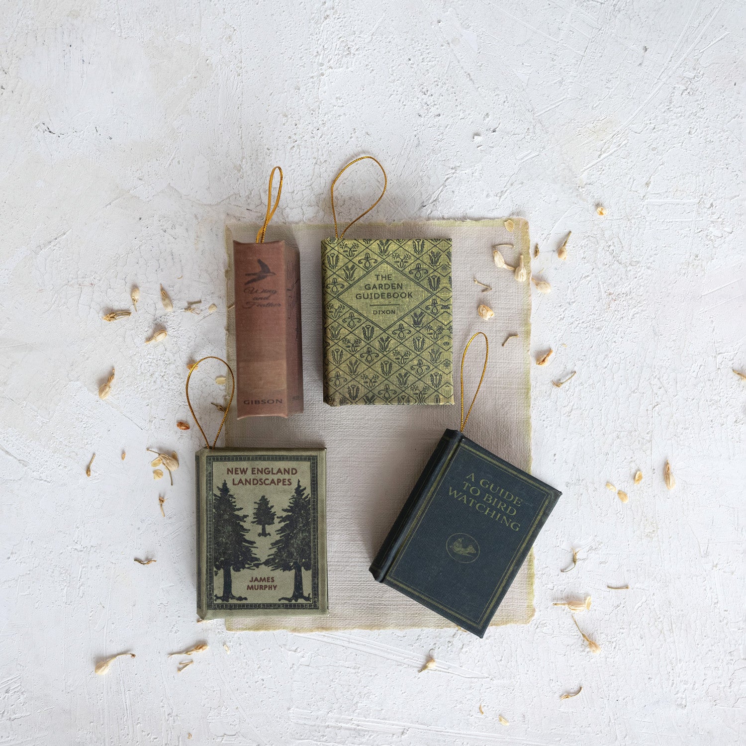 Four assorted vintage-style fabric book ornaments with gold hanging loops on a white background.