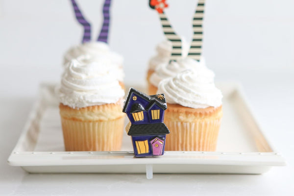 Spooky Spaces haunted house ceramic topper on a white tray with Halloween cupcakes.