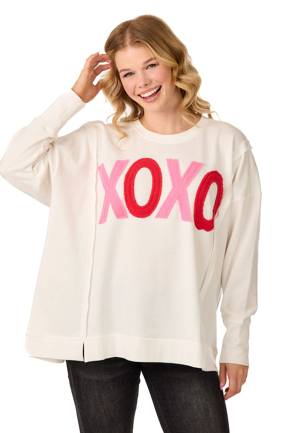 Woman wearing a white French terry XOXO sweatshirt with pink and red bouclé appliqué.