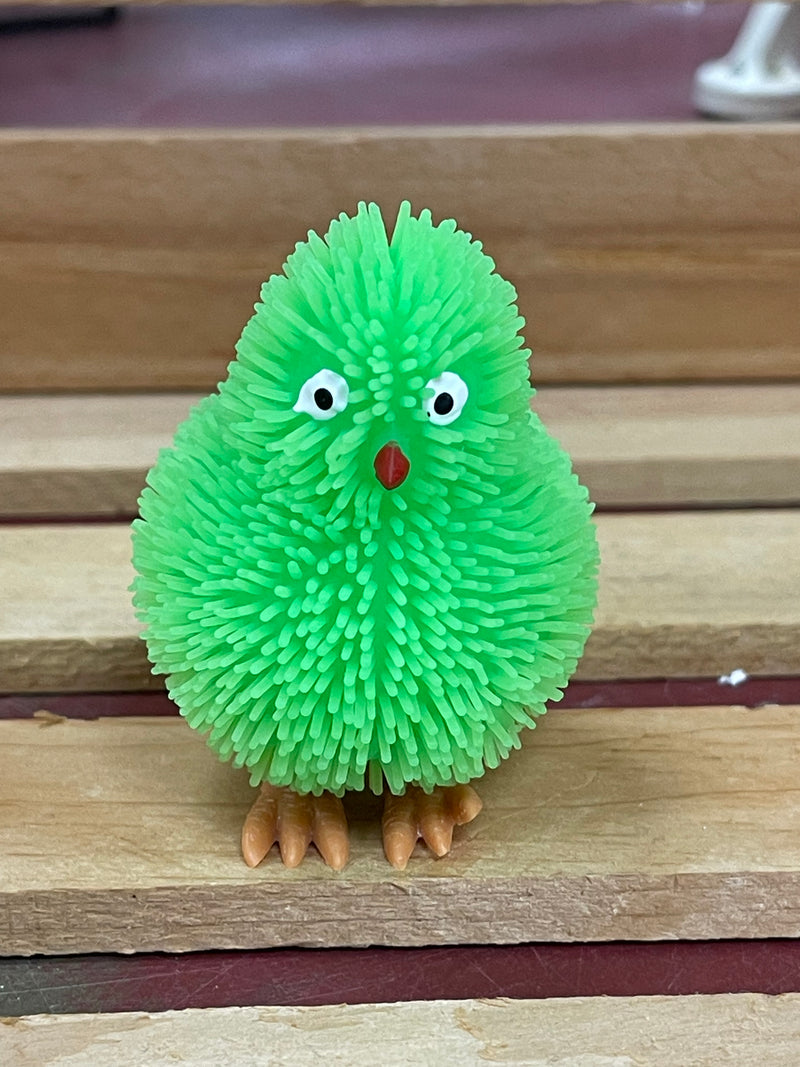 Green puffer chick toy with soft rubbery spikes, white eyes, a red beak, and orange feet.