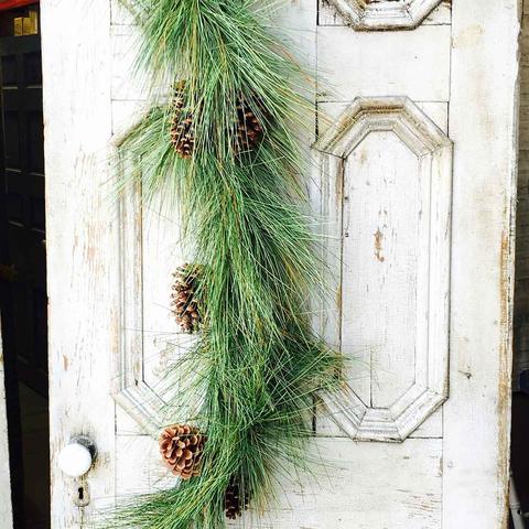 6-foot giant pine and sugar cone garland draped vertically on a rustic white paneled door.
