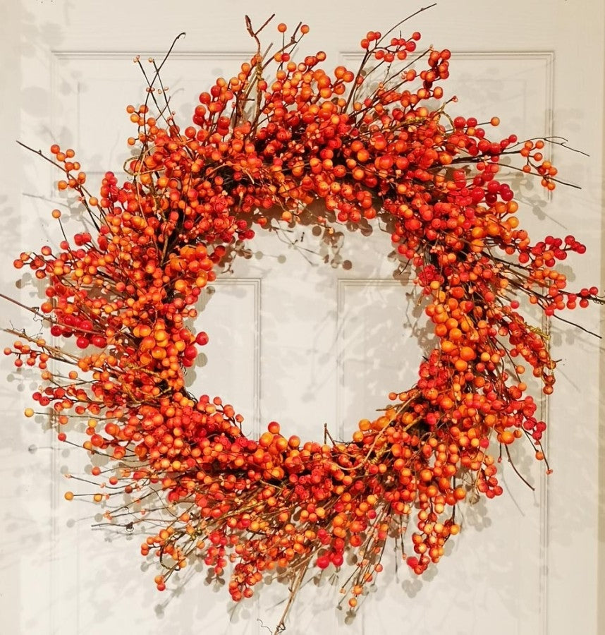 A round decorative wreath made of dense orange and red berries on thin brown branches.